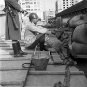 Brigadiano uniformizado de capacete, sentado em seu posto com uma arma posicionada para a rua, no terraço do Palácio Piratini. Atrás dele, em pé, tem outro oficial cujo rosto não aparece na foto.