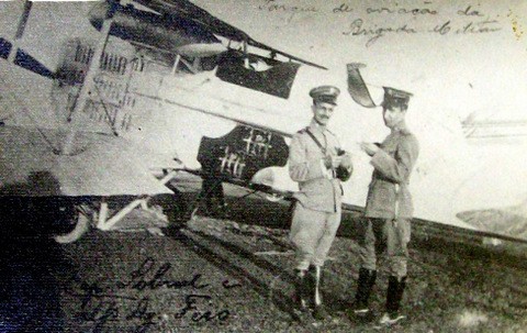 Dois homens posando para um foto na lateral de um avião em solo