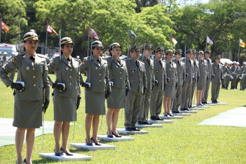 Grupo de 14 oficiais da brigada perfilados lado a lado, em pé sobre pequenas bases quadradas brancas, sobre um gramado