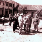 Ildo Meneghetti junto a grupo de homens uniformizados, com outras pessoas ao fundo da foto, no pátio da sede do 2º Batalhão Policial.