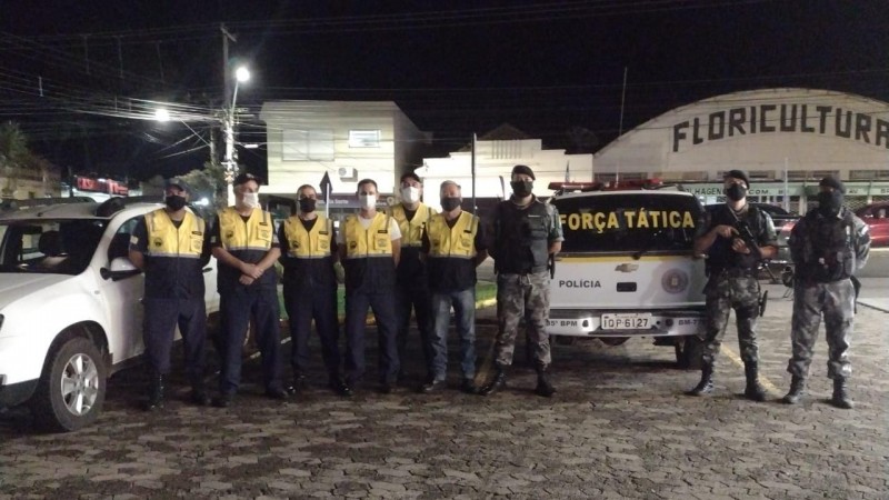 Três policiais militares da força tática a frente de uma viatura policial, e ao lado seis agentes de trânsito perfilados.