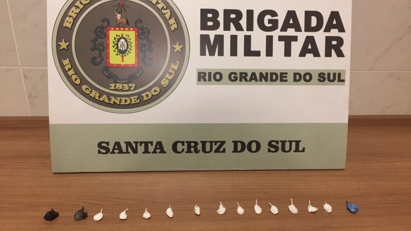 Quinze porções fracionadas de droga e atrás o banner institucional de Brigada Militar de Santa Cruz do Sul