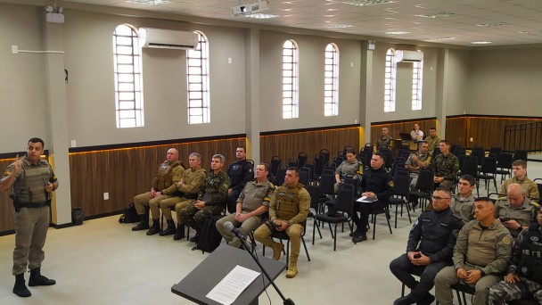 Foto mostra um salão ocupado por vários homens fardados que prestam atenção a uma palestra