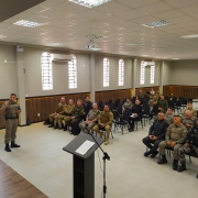 Foto mostra um salão ocupado por vários homens fardados que prestam atenção a uma palestra