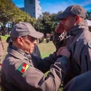 Foto mostra o primeiro colocado recebendo uma medalha de reconhecimento ao mérito.