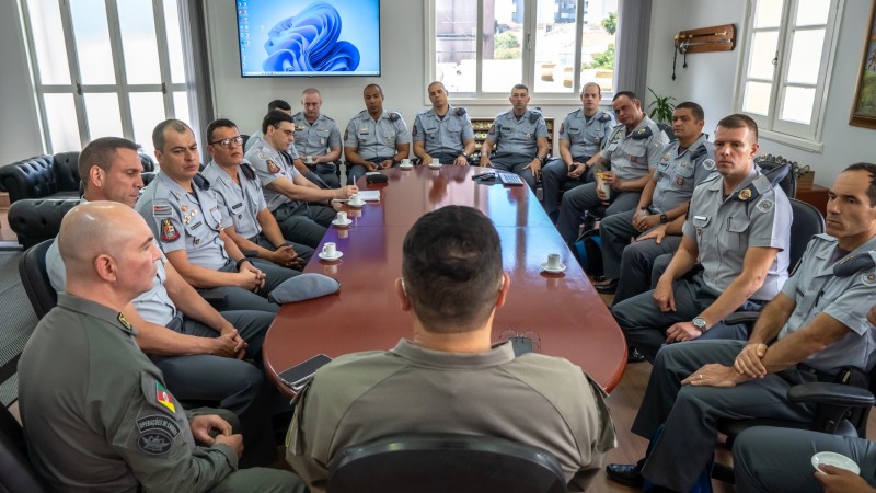 A foto mostra praticamente todos os integrantes da reuni&atilde;o da comitiva com o Comando-Geral da BM. Todos os PMs usam farda e sobre a mesa de trabalho est&atilde;o x&iacute;caras de caf&eacute; e aparelhos celulares. 