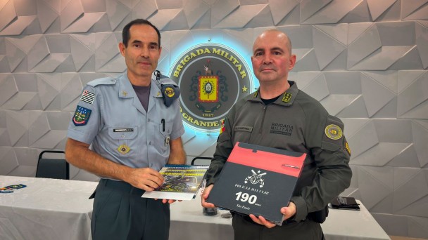 Os dois PMs estão lado a lado e segurando os presentes que trocaram. 