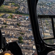 Imagem a&eacute;rea de um bairro feita do interior de um helic&oacute;ptero. Aparece um PM armado no lado esquerdo. 