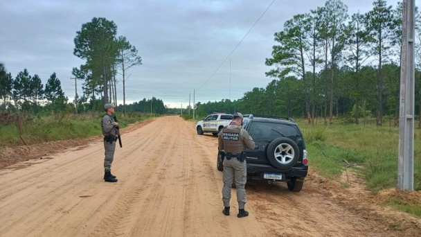 Dois PMs aparecem durante a fiscaliza&ccedil;&atilde;o de um ve&iacute;culo em uma estrada de ch&atilde;o no interior do RS. Ao fundo v&ecirc;-se uma viatura da BM. 