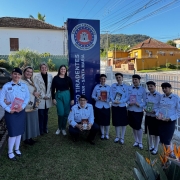Estudantes e servidores em fileira posam para a foto em frente ao CT em dia ensolarado. 
