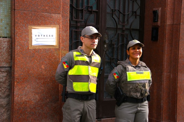 Imagem mostra dupla de soldados posicionados em frente a um prédio público. Ao lado de ambos, uma placa "votação" fixada na parede.