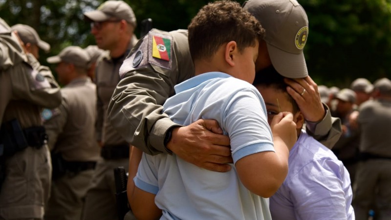 Policial Militar recebe o cumprimento de duas crian&ccedil;as com um abra&ccedil;o emocionado. 